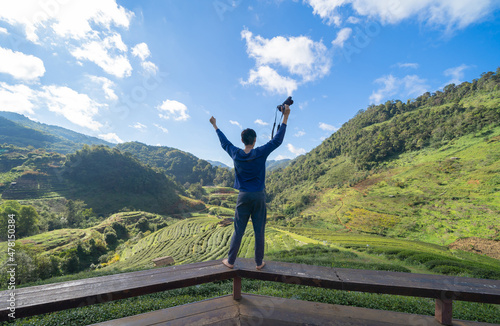 A tourist, a photographer holding a camera, travelling in holiday vacation with forest trees and green mountain hills. Nature landscape background, Thailand. People lifestyle.