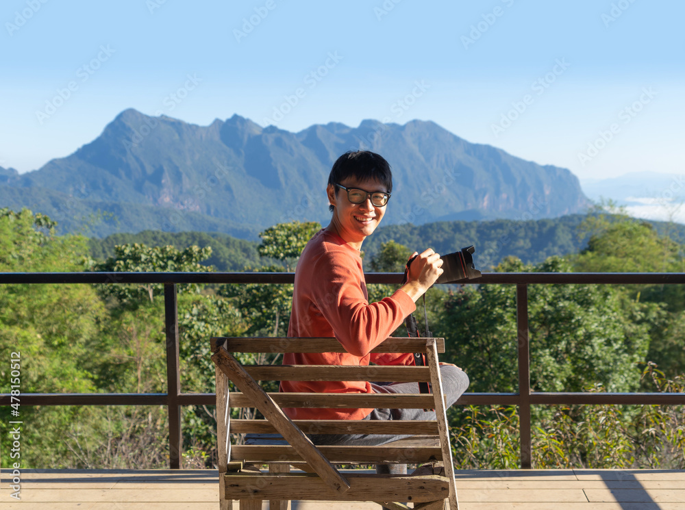 A tourist, a photographer holding a camera, travelling in holiday vacation with forest trees and green mountain hills. Nature landscape background, Thailand. People lifestyle.