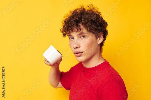 Young curly-haired man in a red T-shirt with a white cap in his hands isolated background unaltered