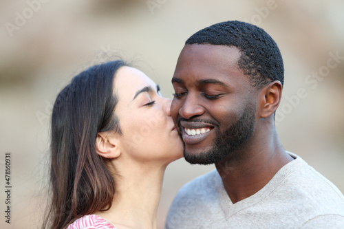 Caucasian woman kissing on cheek a man with black skin