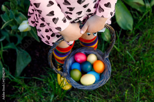 Photography Close-up of legs of toddler girl with colorful stockings and shoes and basket with colored eggs