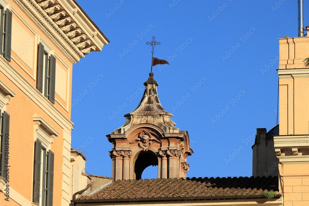 Church Spire with Sculpted Angel Head Against a Bright Blue Sky in Rome, Italy