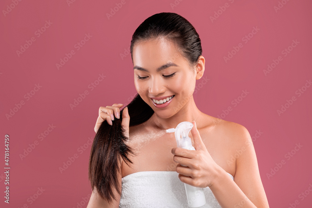 Happy long-haired young asian woman using hair spray Happy long-haired young asian woman using hair spray