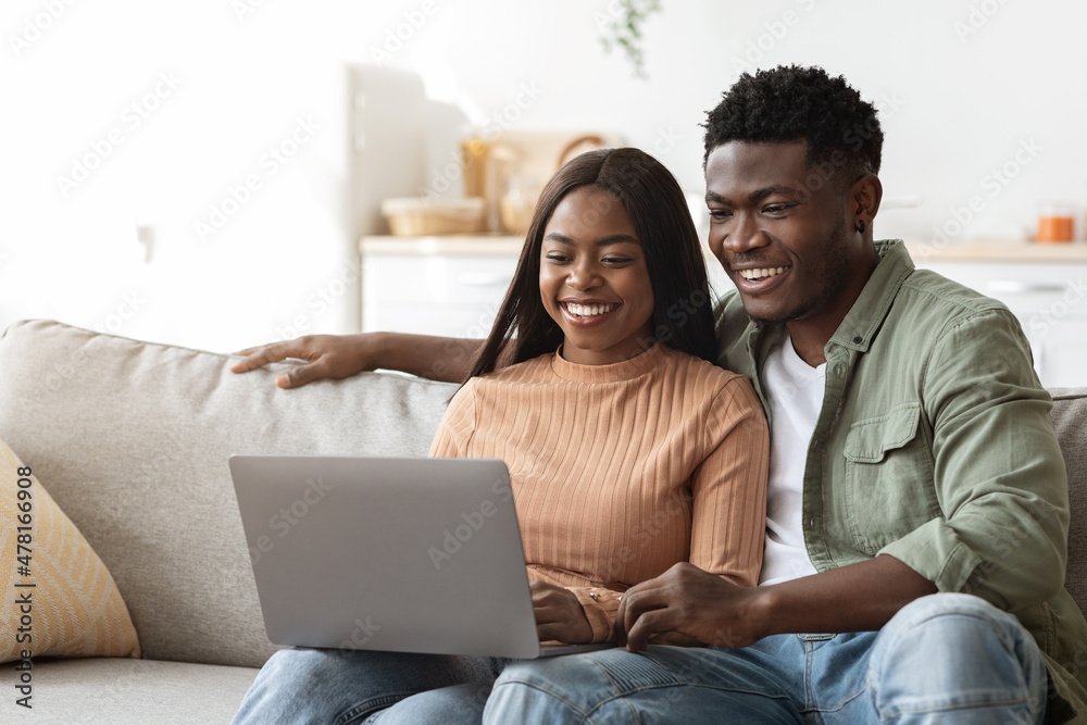 Relaxed african american young couple enjoying weekend together, using laptop Relaxed african american young couple enjoying weekend together, using laptop
