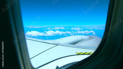 View through the window of the airplane during a flight, seeing the wing and the turbine. Plane trip on a beautiful blue sky day, concept of vacation trip.