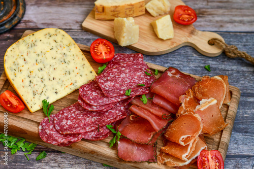 Italian dried thinly sliced artisan pork salami Milano , mediterranean parmesan cheese, tomatoes and fresh basil on wooden background .Rustic home made italian snack.