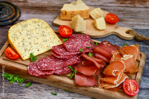 Italian dried thinly sliced artisan pork salami Milano , mediterranean parmesan cheese, tomatoes and fresh basil on wooden background .Rustic home made italian snack.