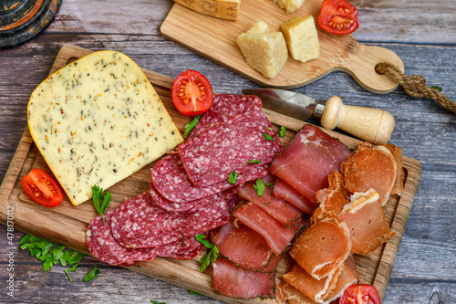 Italian dried thinly sliced artisan pork Salami Milano , mediterranean Parmesan cheese, tomatoes and fresh basil on wooden background .Rustic home made Italian snack.