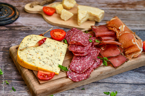 Italian  dried thinly sliced   artisan  pork Salami Milano ,  mediterranean Parmesan cheese, tomatoes   and fresh basil on wooden background .Rustic  home made Italian snack.