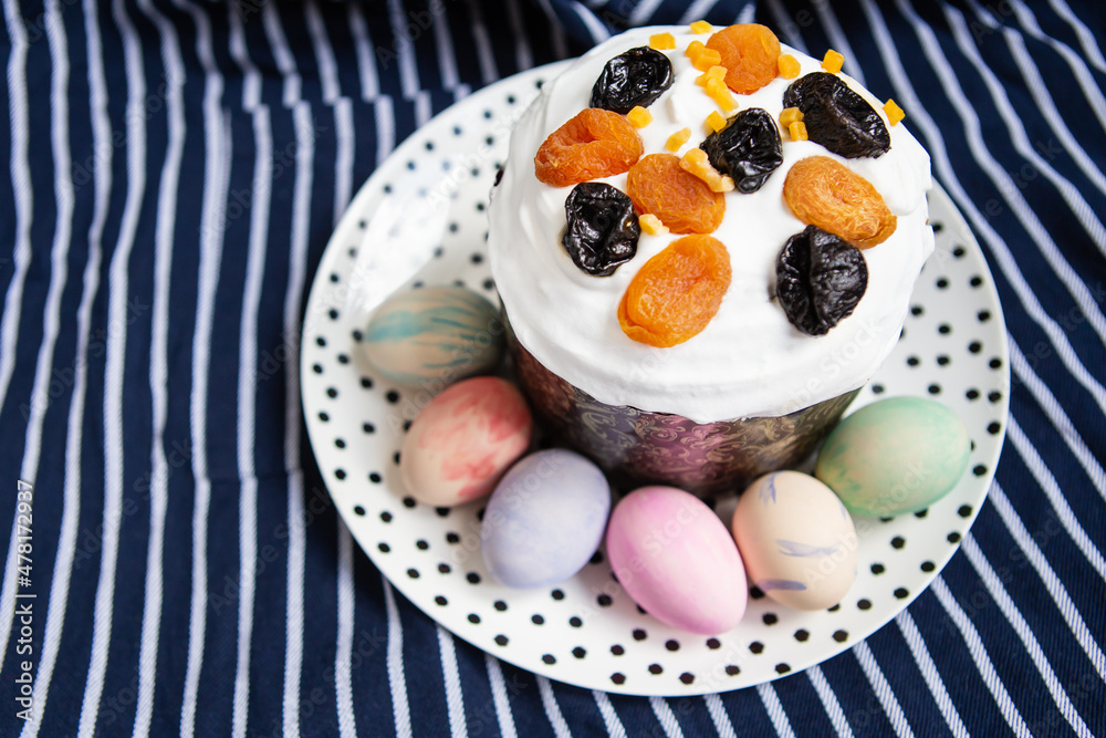 Easter eggs and Easter cake lie on a plate lying on a striped blue apron. Easter religious holiday concept. Easter eggs and Easter cake lie on a plate lying on a striped blue apron. Easter religious holiday concept.