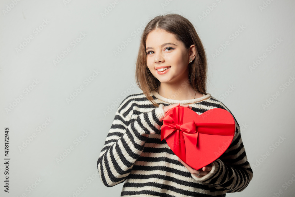 Beautiful girl in striped sweater with heart shape gift box on white background