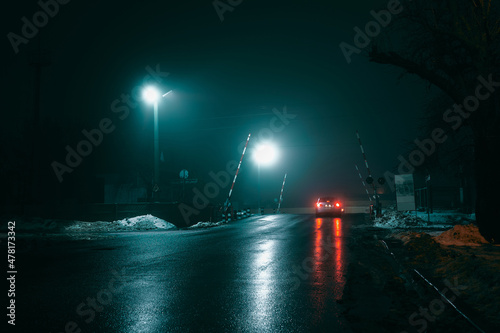 Car at a railway crossing at night during fog, winter