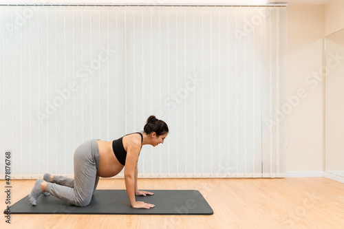 A pregnant woman kneeling on a mat doing yoga at health center