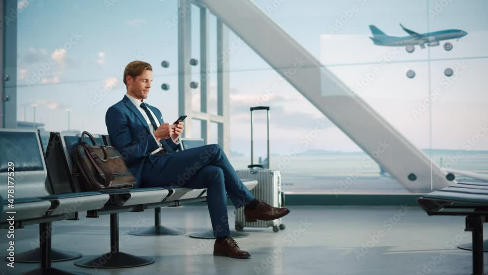 Airport Terminal: Businessman Uses Smartphone, Waiting for a Flight, Doing e-Business, Sending e-Commerce Data. Traveling Man Remote Work Online on Mobile Phone in Boarding Lounge of Airline Hub Airport Terminal: Businessman Uses Smartphone, Waiting for a Flight, Doing e-Business, Sending e-Commerce Data. Traveling Man Remote Work Online on Mobile Phone in Boarding Lounge of Airline Hub