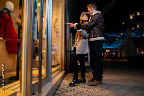 Young lovely couple looking store windows at night while walking through the city 