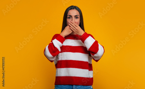Don't speak! Serious sad young woman is covering her mouth with hands help and looking straight on camera