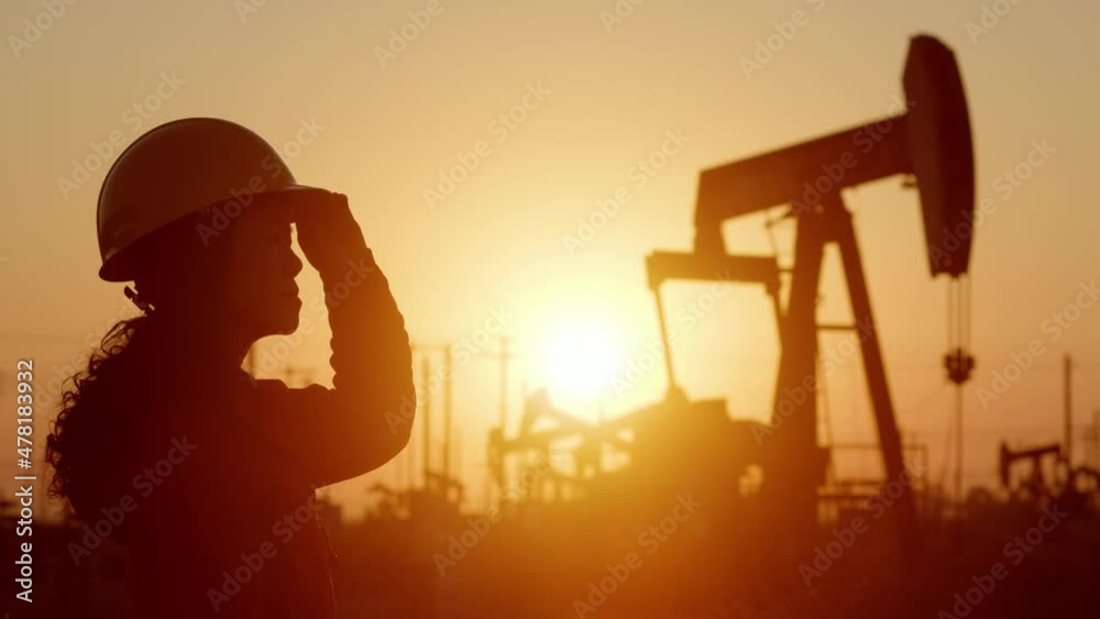 An Asian woman engineer inspects oil pumps at sunrise in a large oil field in California.