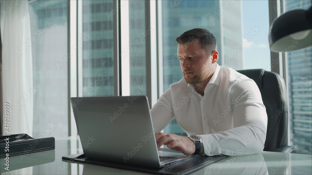 Businessman behind a laptop in the office. A businessman in a white shirt sits at a table in a skyscraper. Businessman behind a laptop in the office. A businessman in a white shirt sits at a table in a skyscraper.