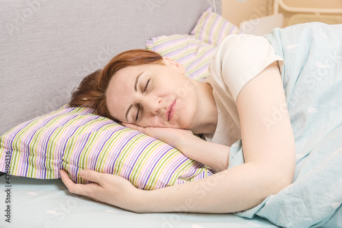 Forty-year-old woman sleeping on her side after a hard day at work. Restoring strength during sleep. Home bedroom interior, rest time, sound sleep.