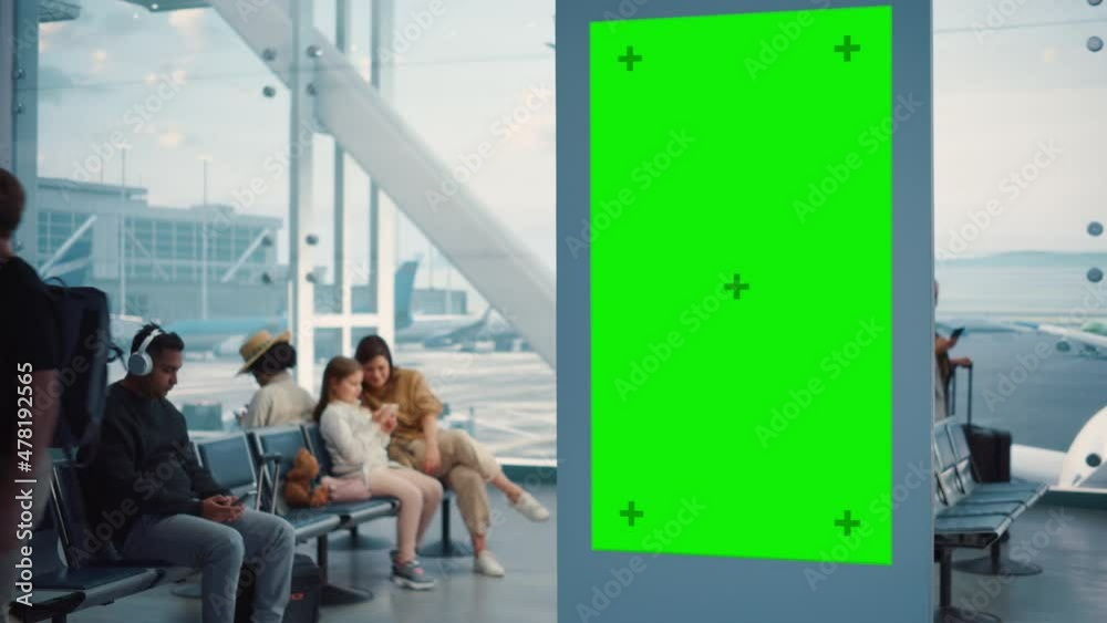 Airport Terminal: Green Screen Advertising Billboard, Arrival Display with Chroma Key, Mock-up AD Space. Backgrond: Diverse Crowd of People Wait for their Flights in Boarding Lounge of Airline Hub