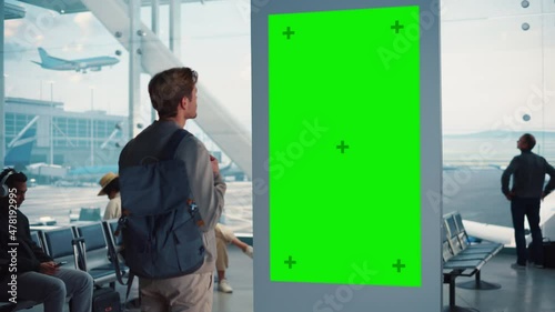 Airport Terminal: Young Man Looking for His Fligt at Green Chroma Key Screen Arrival Departure Information Display. Backgrond: Diverse People Wait for their Flights in Boarding Lounge of Airline Hub photo