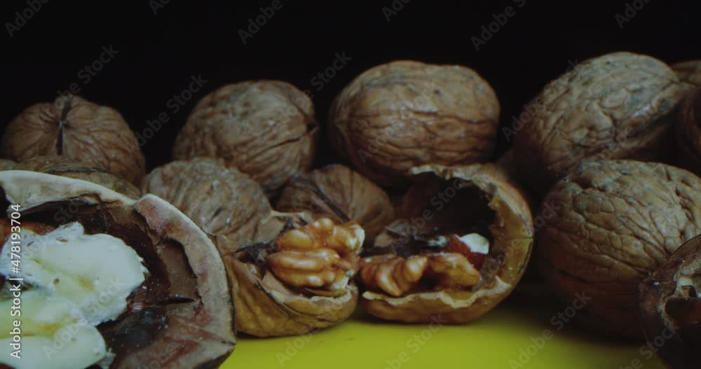 Close-up Shot of Walnuts which lie on a yellow table against a black background. Close-up camera travel along the lying nuts as close as possible to the chopped walnut. Close-up Shot of Walnuts which lie on a yellow table against a black background. Close-up camera travel along the lying nuts as close as possible to the chopped walnut.