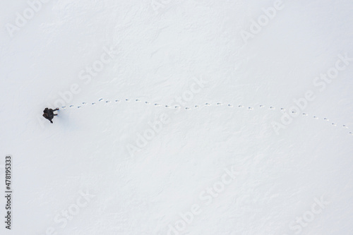 a woman walks through fresh snow leaving footprints, top aerial view, winter outdoor activity