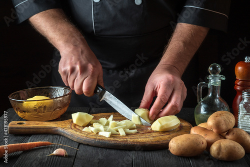 Before preparing the national dish, the chef cuts raw potatoes into small pieces with a knife. Close-up of a cook hands while working in a restaurant kitchen