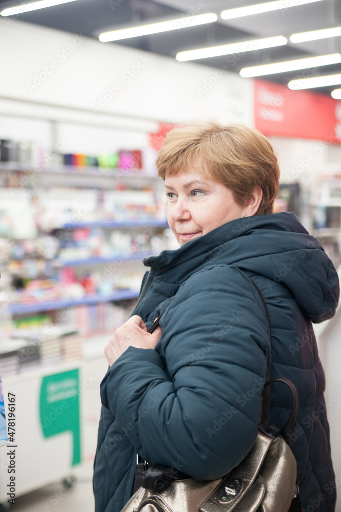  Mature woman in winter clothes among   bookshelves in   store