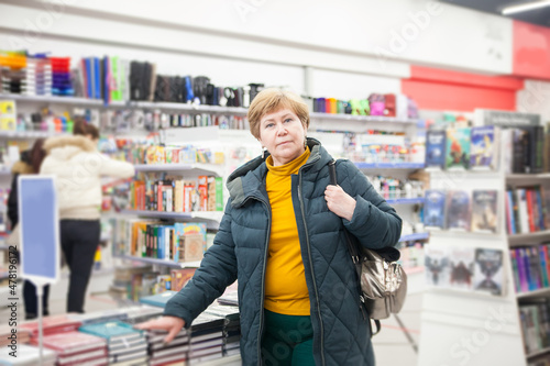  Mature woman in winter clothes among bookshelves in store