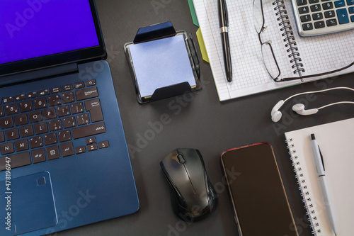 Laptop with mouse, notebook with pen and other accessories on the desktop with a dark surface