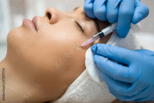 Woman in beauty salon getting botox injections to the cheek, close up