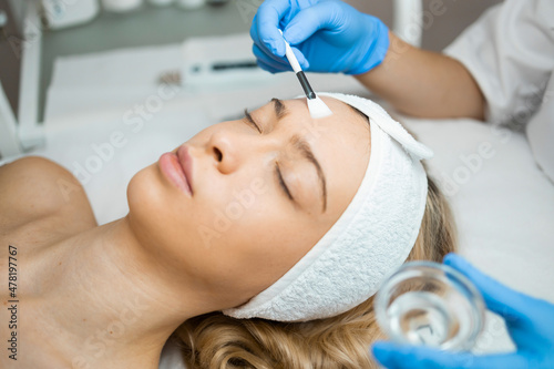 Beautician's hands in blue protective gloves applying a transparent moisturizing peeling mask to a woman's facial skin. Beauty treatments photo