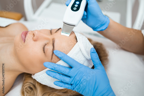 Close up of relaxed woman receives ultrasonic facial cleansing from the hands of a professional cosmetologis. Face skin peeling in a beauty salon