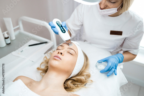 Cosmetologist or dermatologist making ultrasound facial cleaning for woman in beauty salon. Skin care procedure
