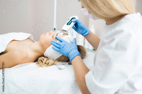 Cosmetologist in blue gloves does ultrasound cleaning of a woman's face. Cleansing and rejuvenating procedure in a beauty salon. Skin peeling