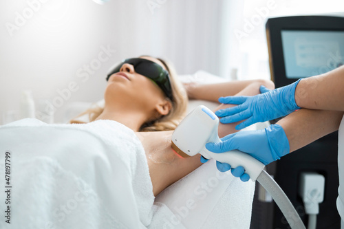 Woman on underarm laser epilation procedure in beauty clinic. Beautician removing hair of pretty blonde armpit photo