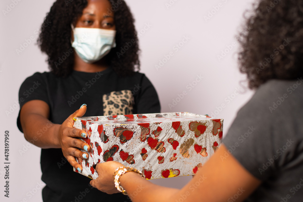 african lady wearing a face mask giving a friend a gift african lady wearing a face mask giving a friend a gift