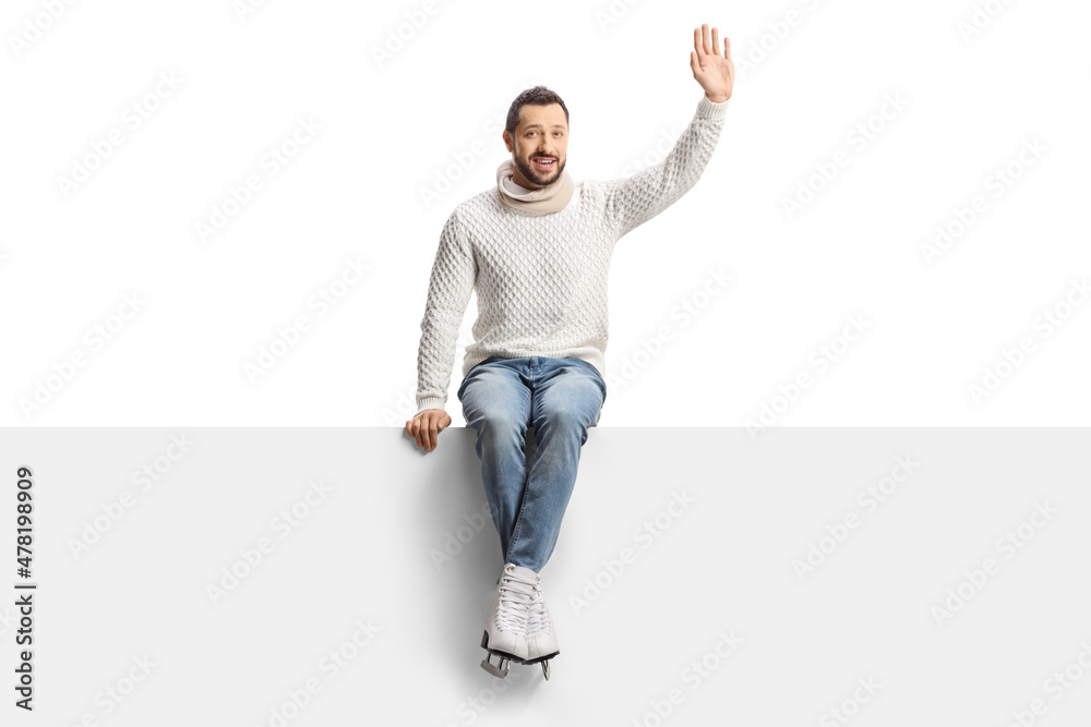 Casual young man with ice skates sitting on a blank panel and waving