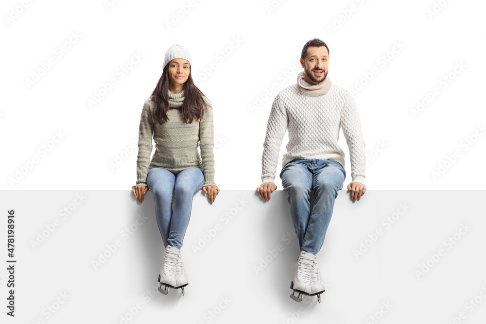 Young man and woman sitting on a blank panel and wearing ice skates Young man and woman sitting on a blank panel and wearing ice skates