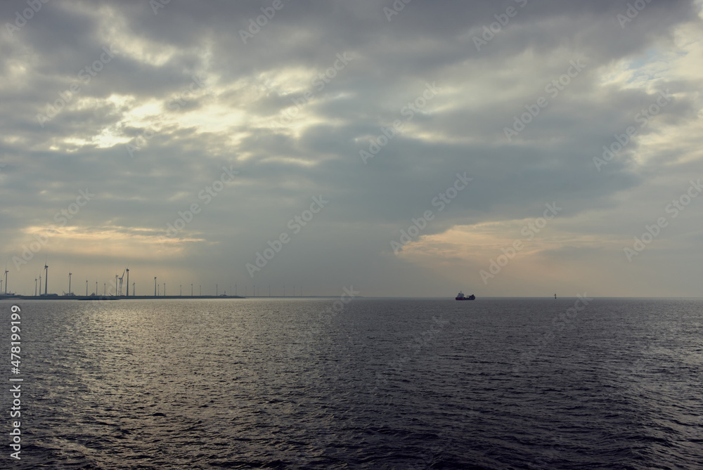 Wind turbine - the sky and the sea, the sun breaks through the clouds, cargo ship at sea