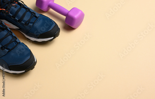pair of blue sneakers and purple dumbbells on a beige background, sports. Copy space