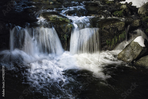 In the heart of the mountains in winter  at night  a river  the water falling on the foamy rocks and the snow on each side