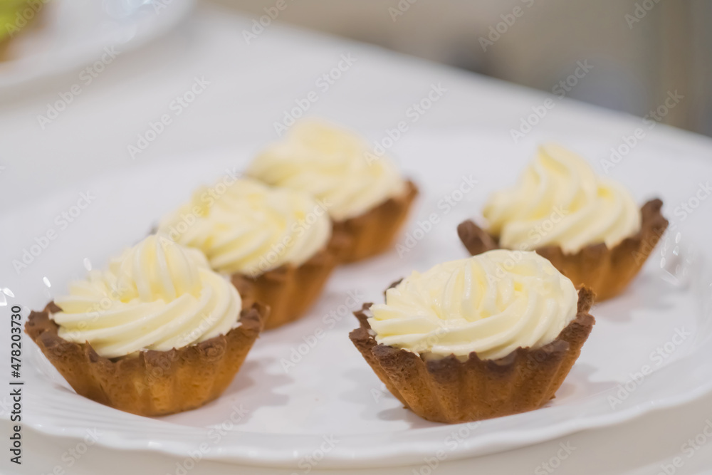 Assortment of delicious fresh shortcrust tart cakes with cream on white plate for sale at restaurant, cafe, bakery. Dessert, culinary, sweet food and confectionery concept