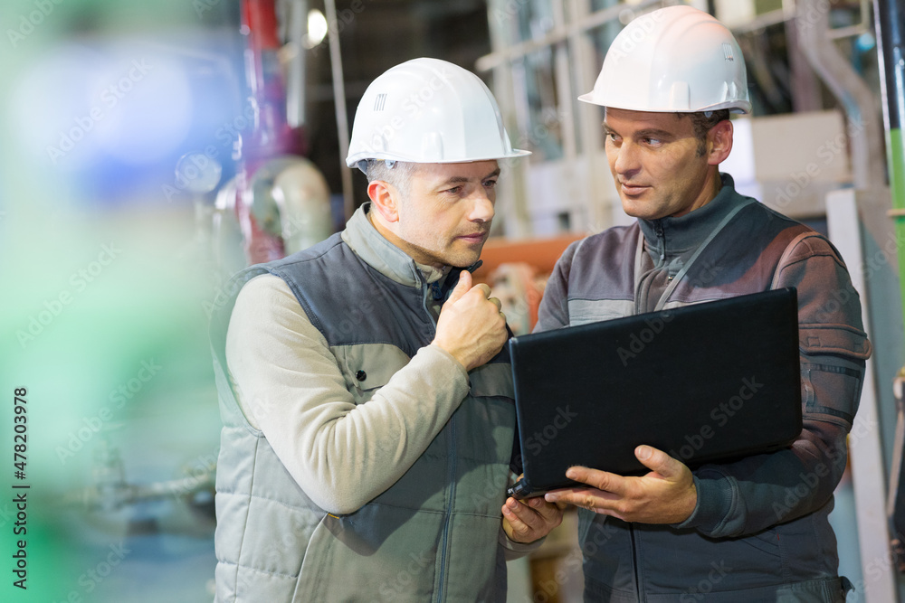 workers with hardhat on looking at the laptop screen workers with hardhat on looking at the laptop screen