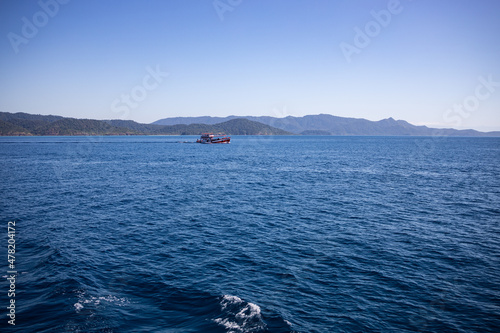 View of a green island on the horizon with boat. Clear sky.