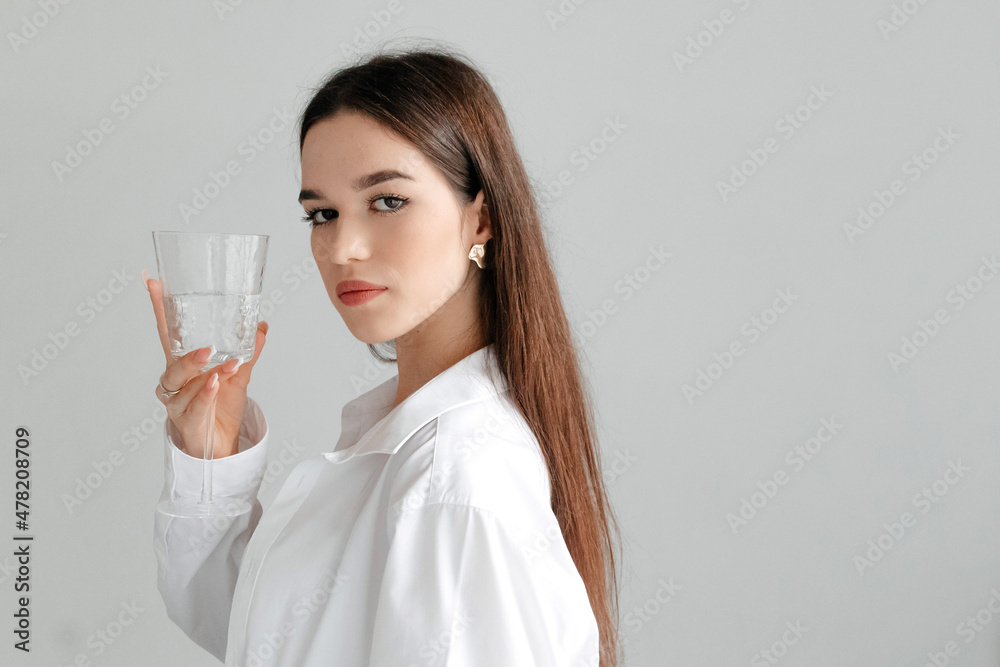 Portrait of a young model raising glass of pure water, looking at the camera, studio portrait on white Portrait of a young model raising glass of pure water, looking at the camera, studio portrait on white