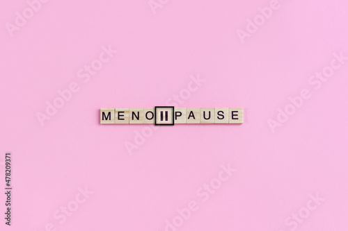 Menopause word and pause sign on wooden blocks with lettering on pink background. Minimal concept of female periods.
