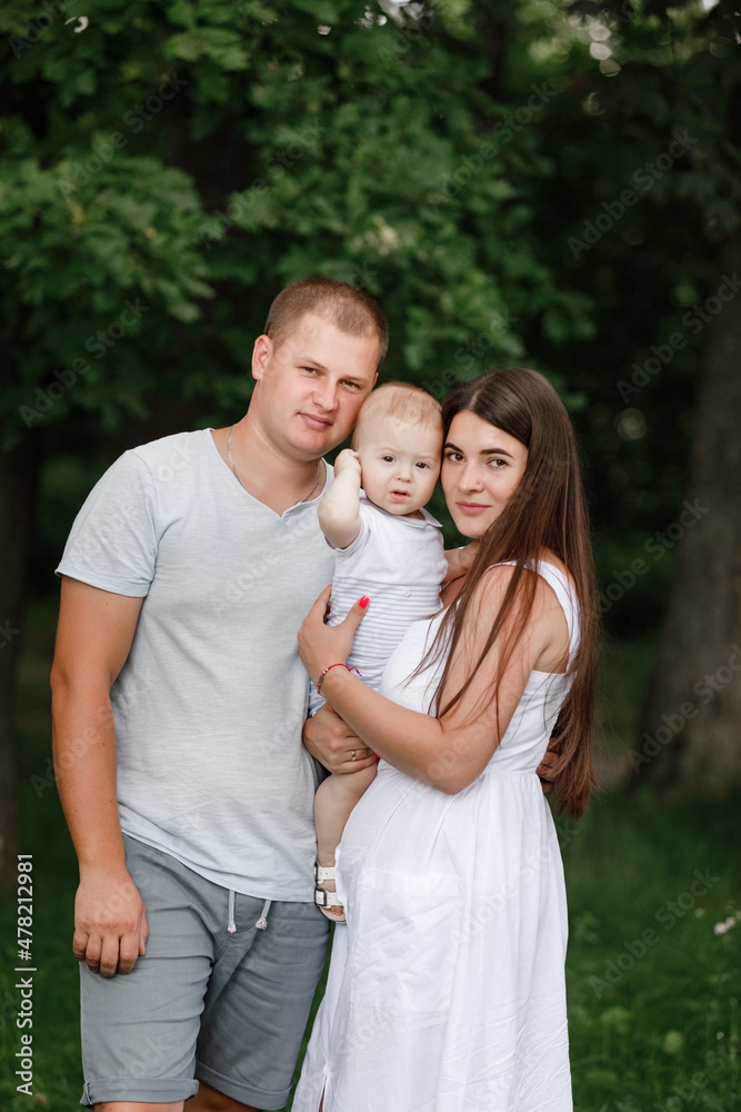 Happy young family, mom, dad and baby son spending time together outdoors in summer green garden