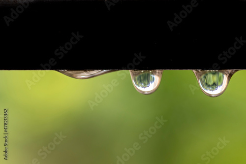 Extreme close-up with selective focus of the rain drops are hanging from a metallic pole. The green garden background in Brazil